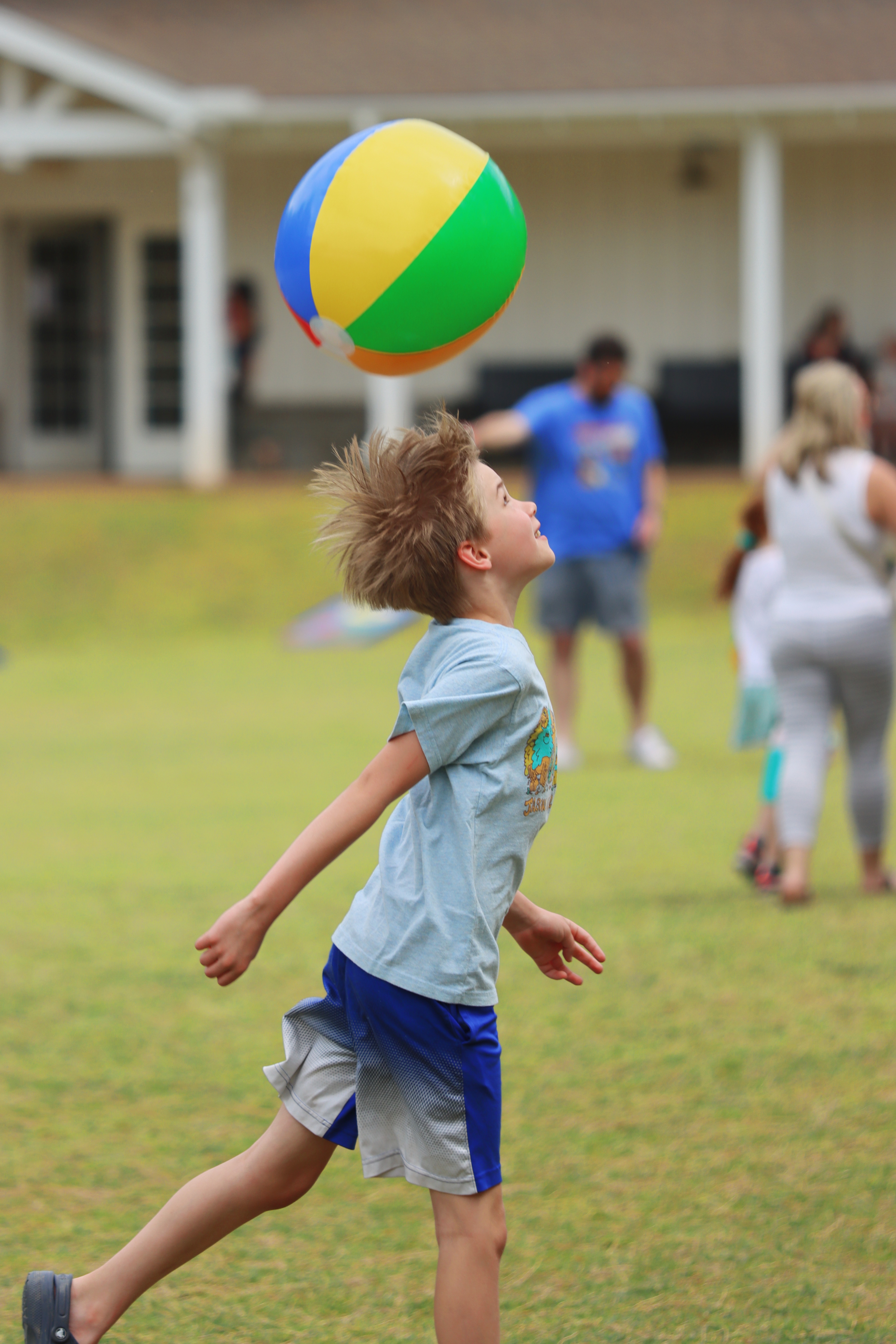 Boy with wild hair leaping to head a beach ball on the lawn