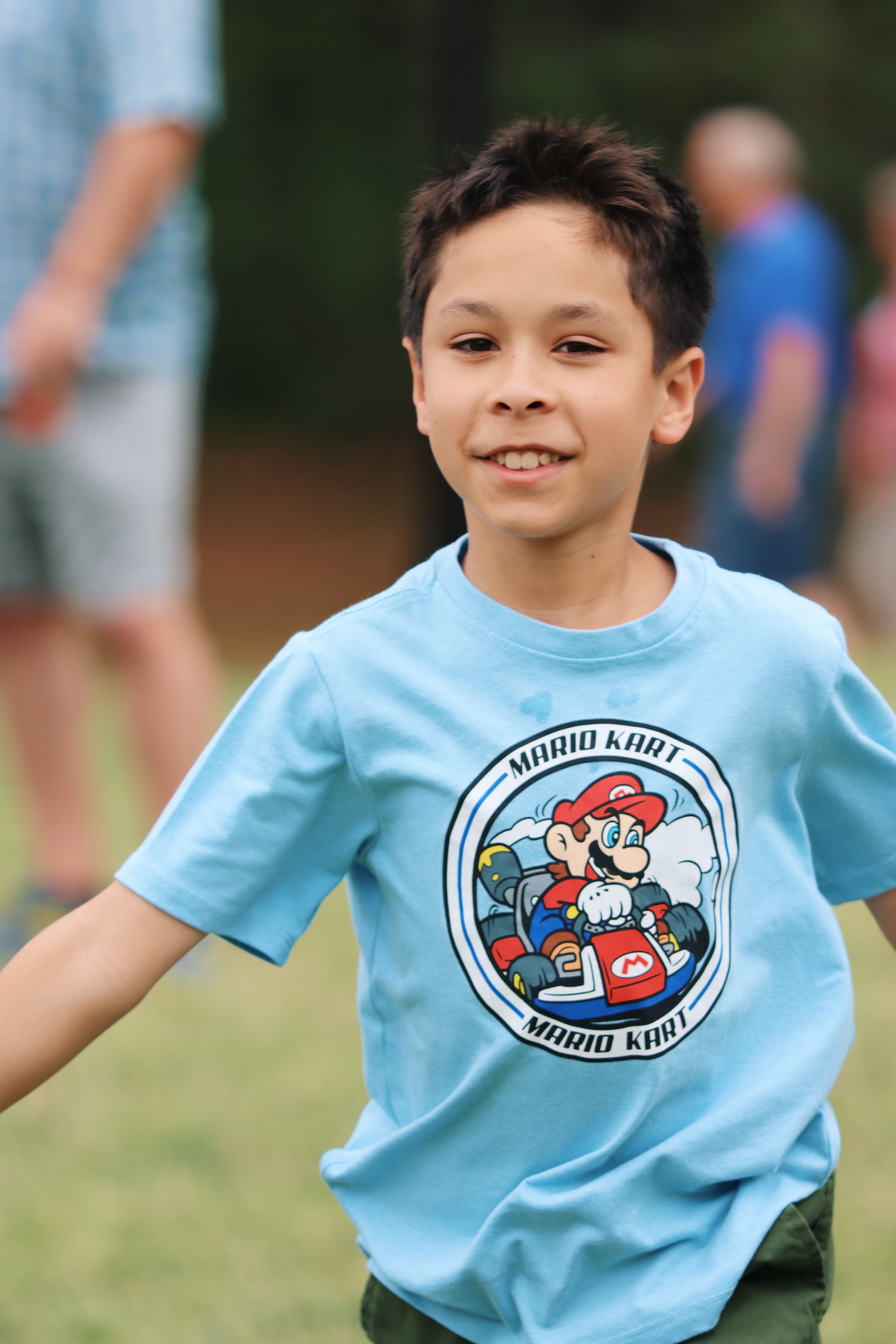 Boy in a Mario Kart shirt running and smiling outdoors