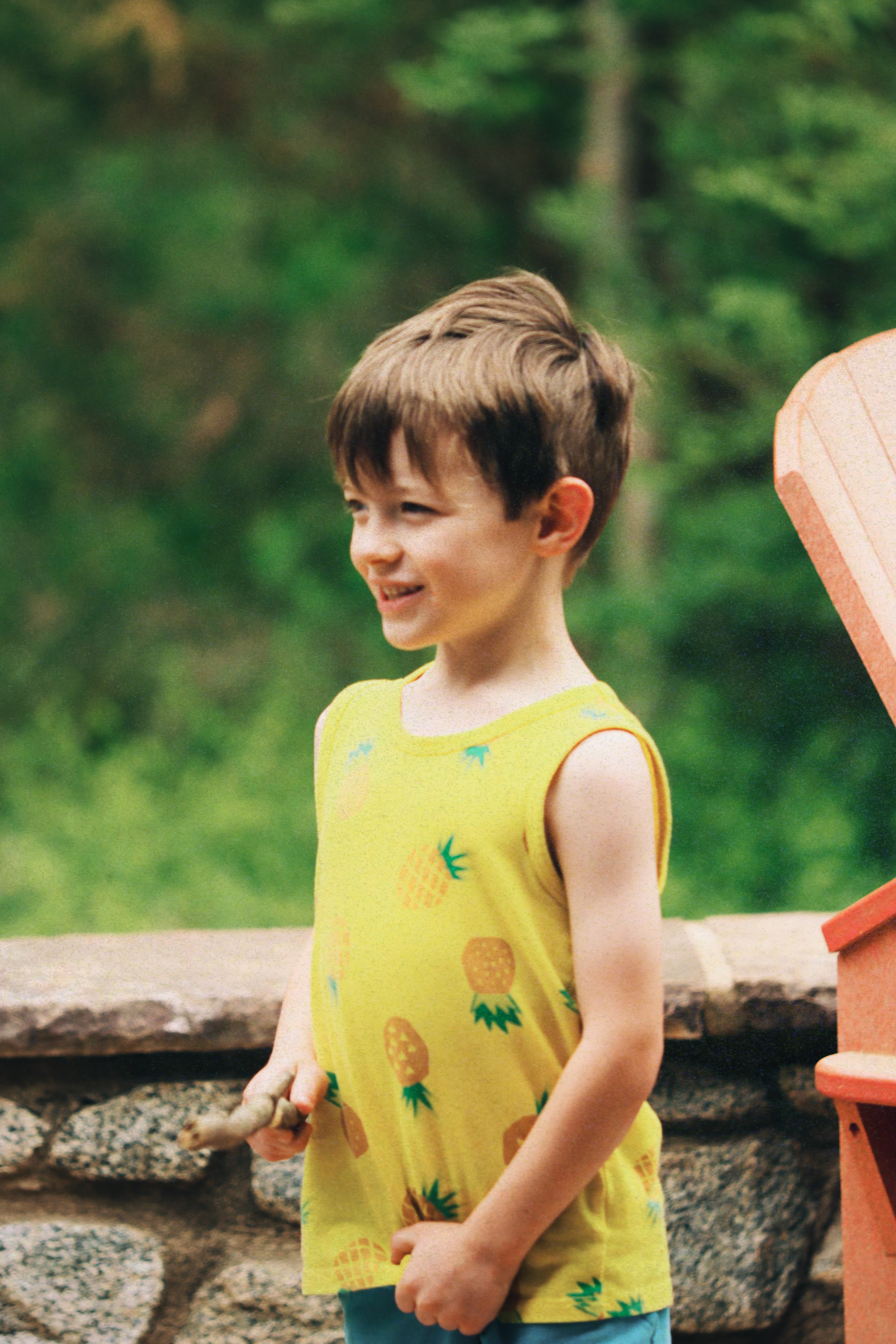 Boy in a yellow pineapple tank top smiling outdoors