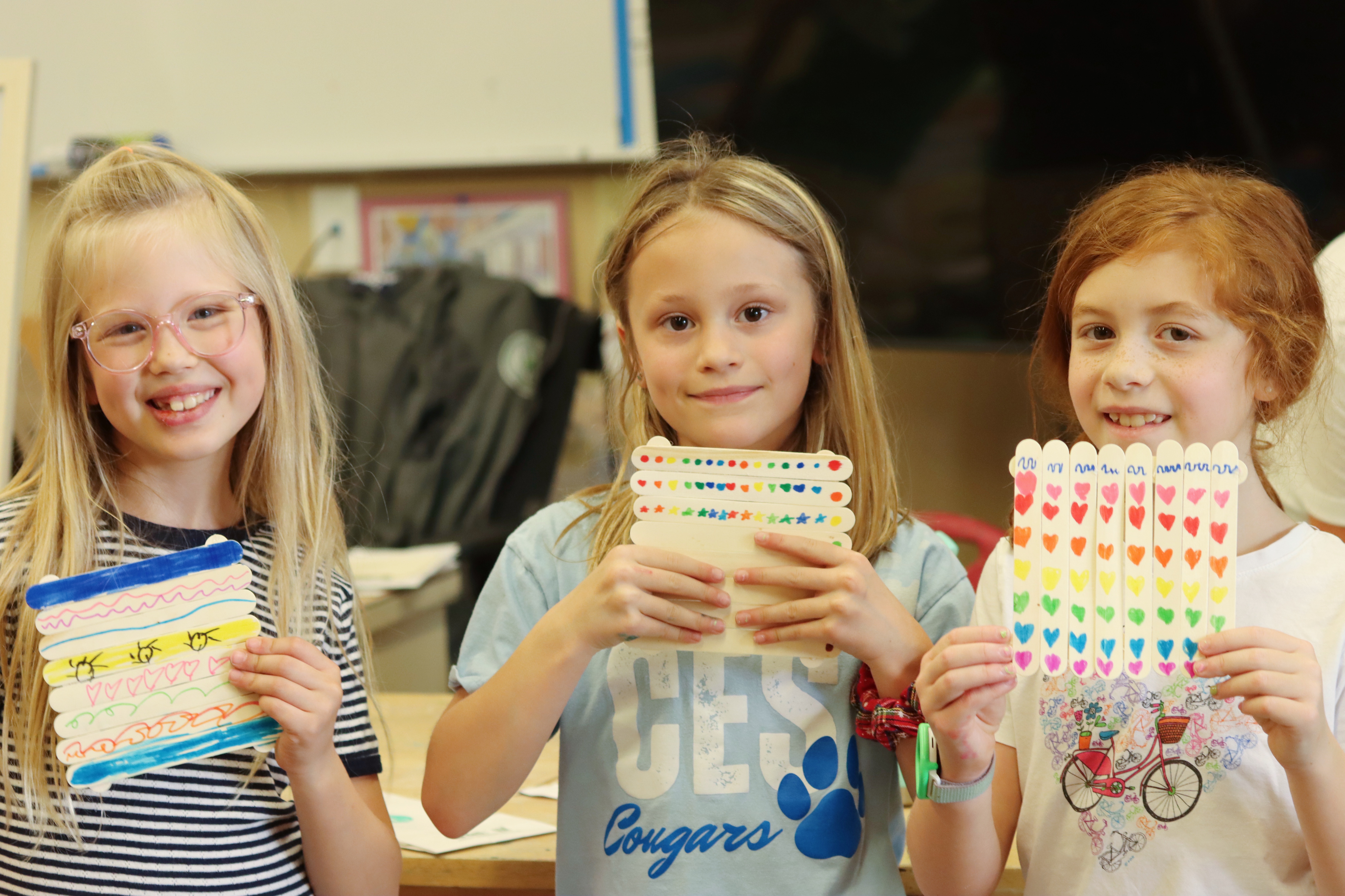 Three girls proudly displaying their decorated popsicle stick art
